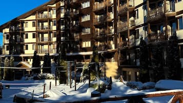 A multi-story hotel with balconies, a ski slope in the foreground, and snow-covered surroundings.