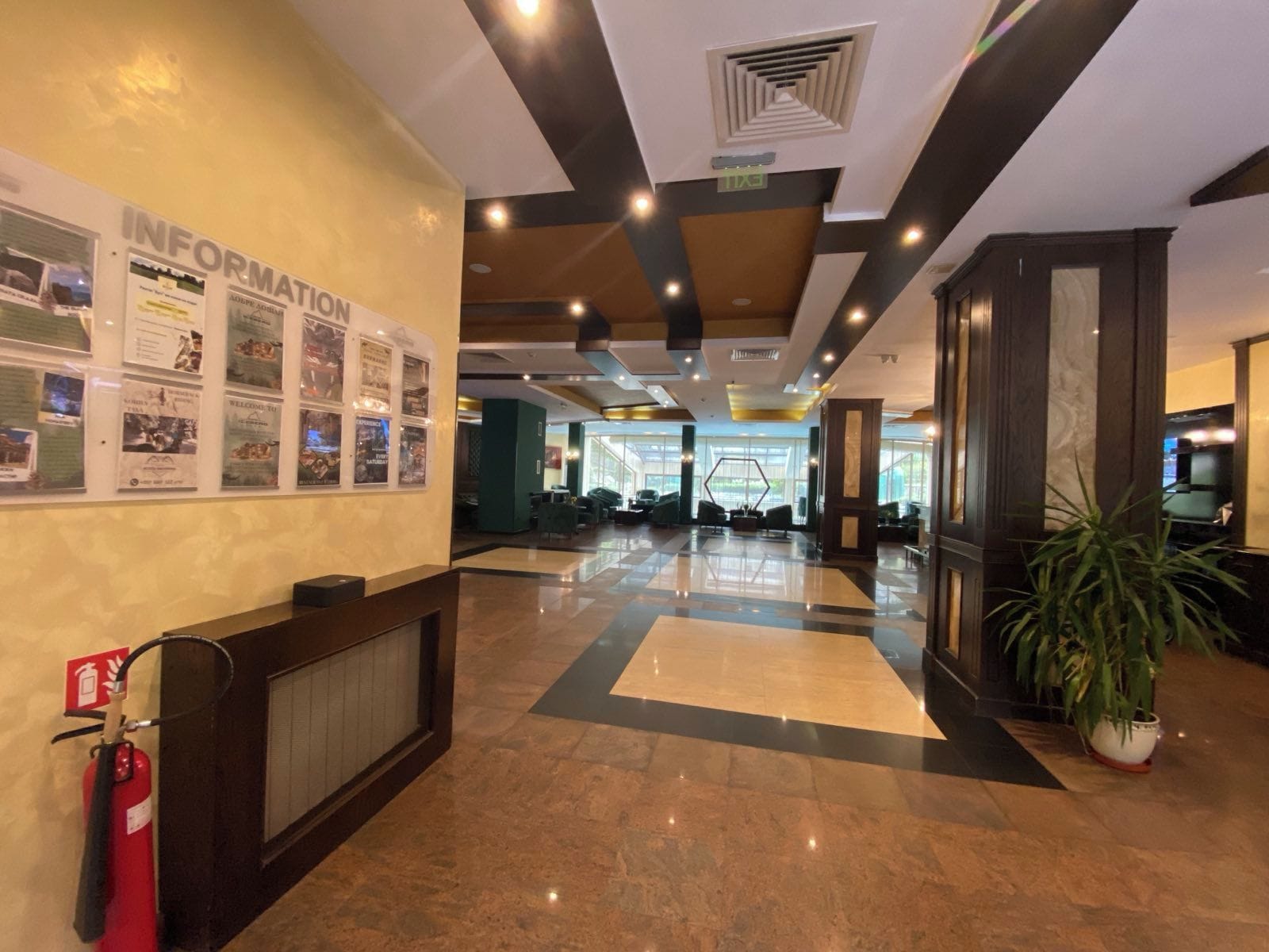 A hotel lobby with a reception desk, information board, and a fire extinguisher.