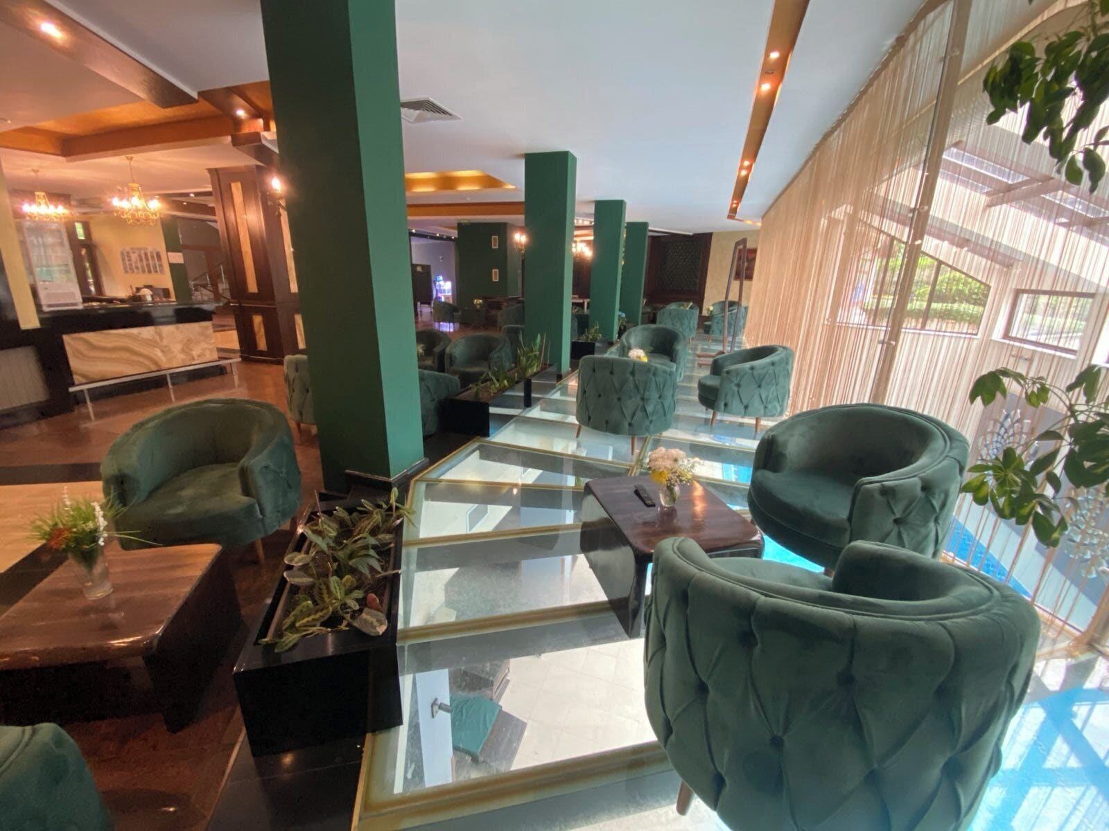 A lobby with green upholstered chairs, a glass coffee table, and a reception desk.