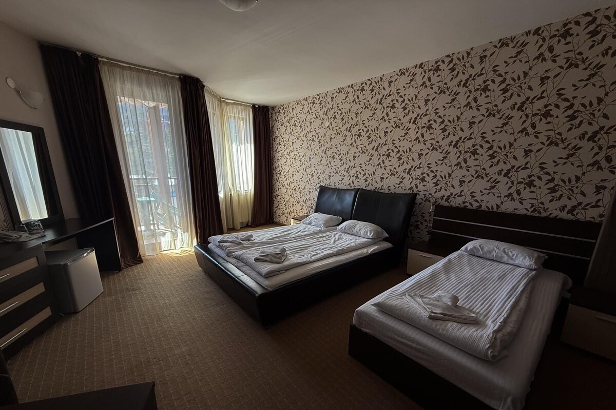 A hotel room with two beds, a desk, and a large window with curtains.
