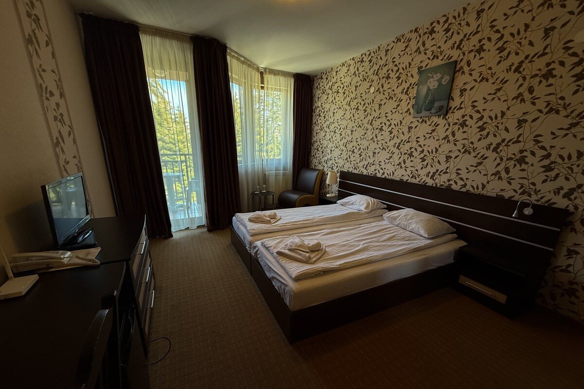 A hotel room with a bed, a desk with a computer, a chair, and a window with curtains.