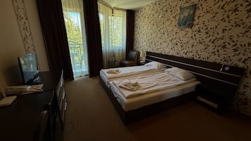 A hotel room with a bed, a desk with a computer, a chair, and a window with curtains.