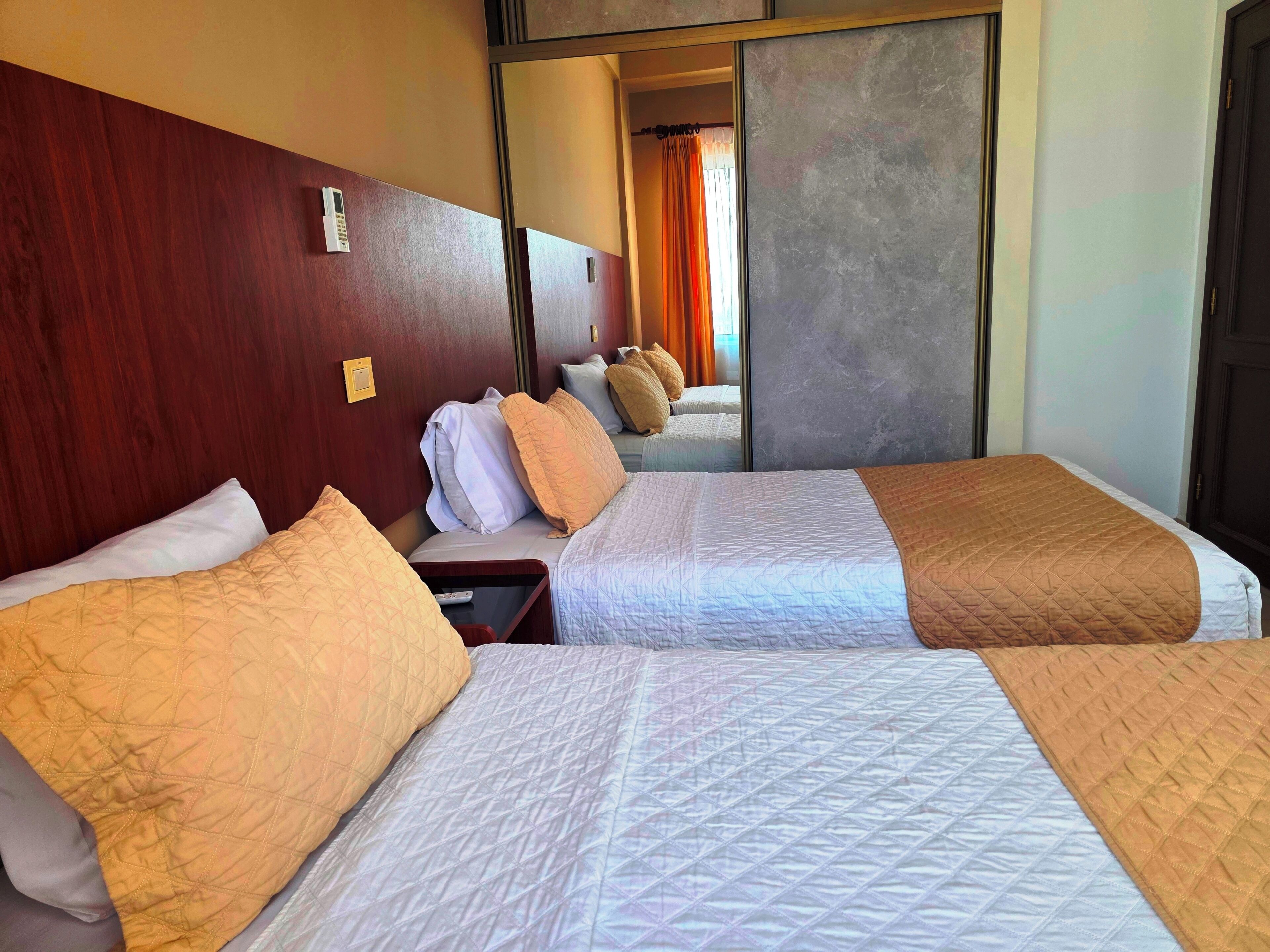 Une chambre d’hôtel avec deux lits, une tête de lit en bois, une table de chevet et un miroir.