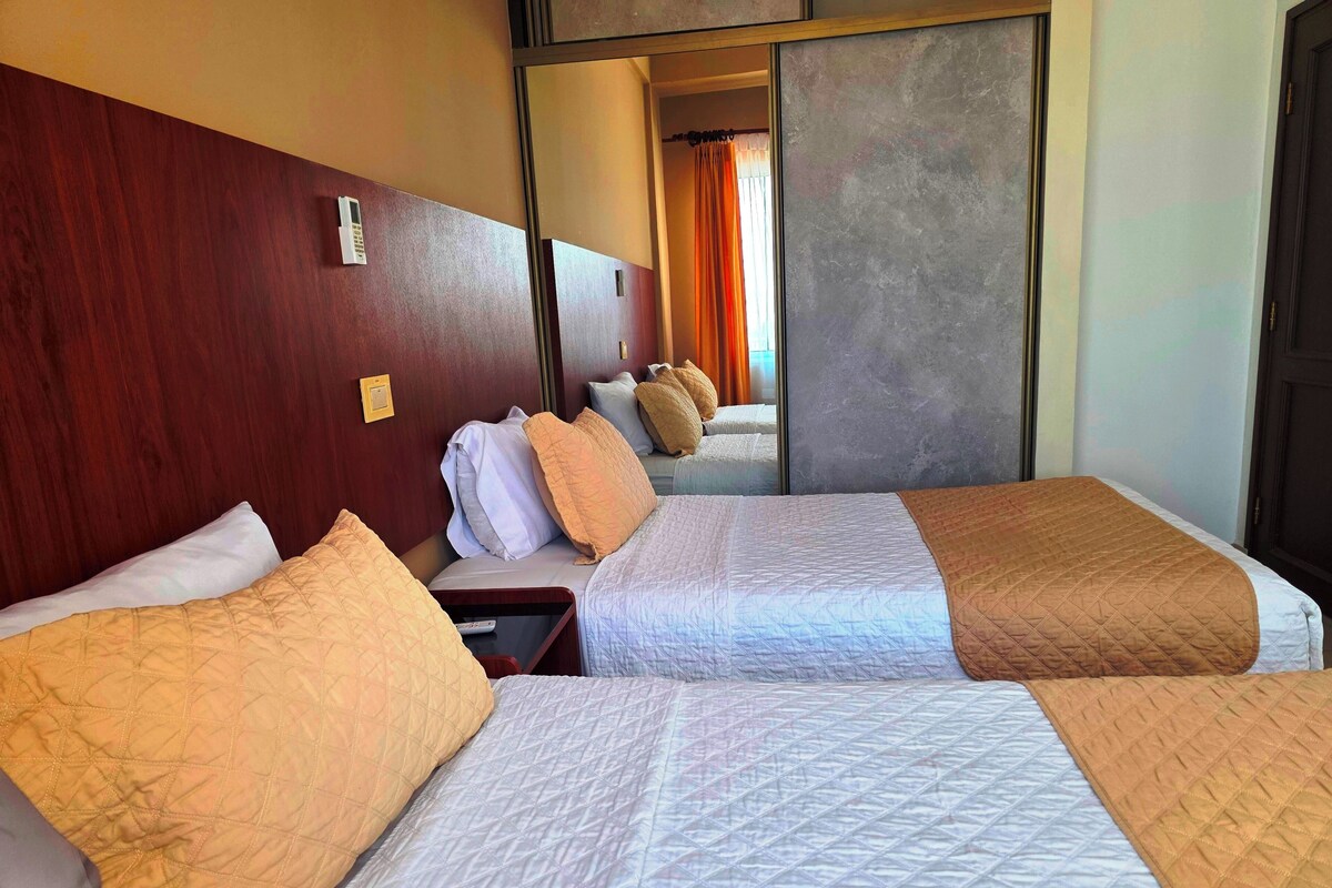 A hotel room with two beds, a wooden headboard, a bedside table, and a mirror.