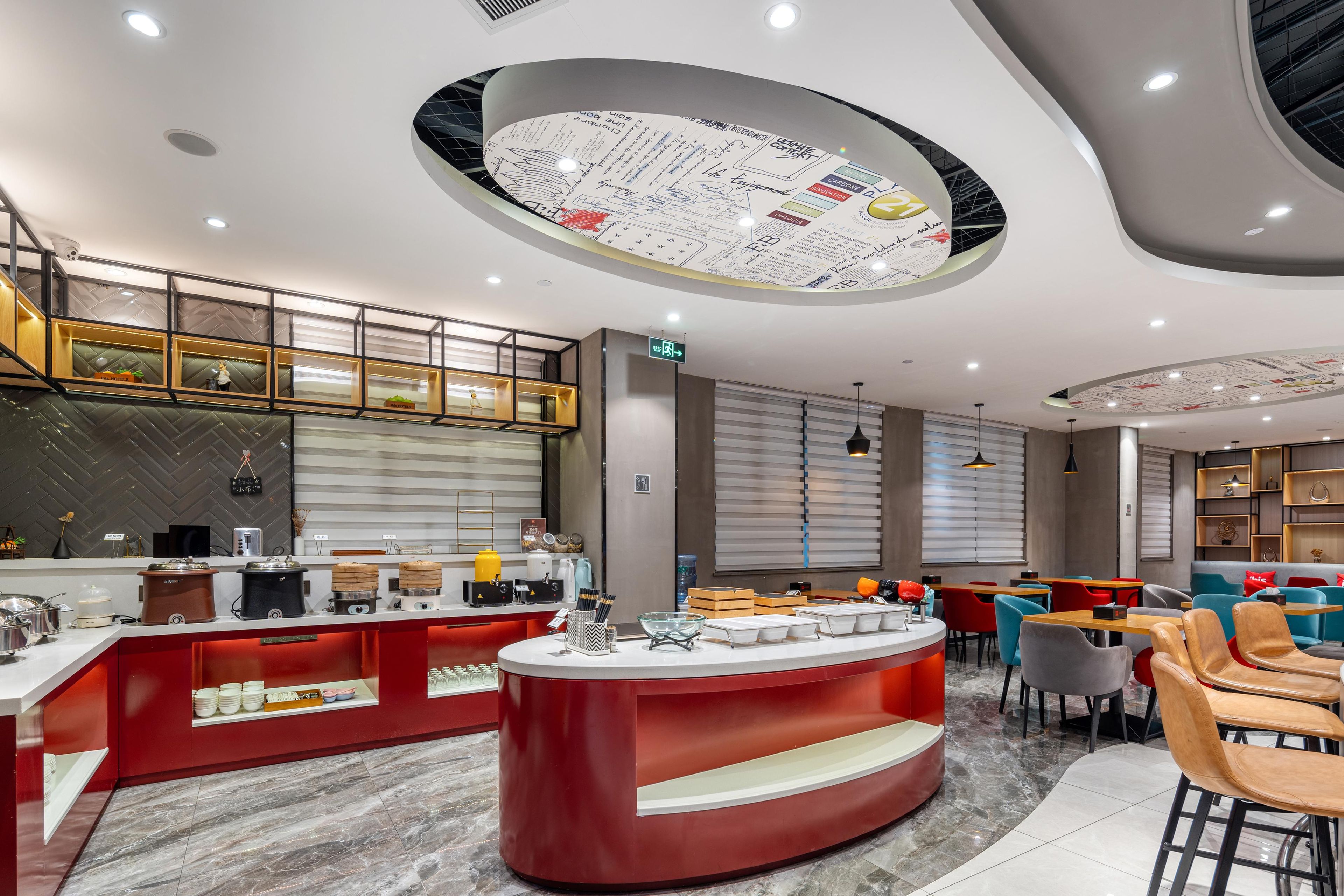 Een modern restaurant met een centraal rode toonbank, een zitgedeelte en een plafond met een cirkelvormig ontwerp.