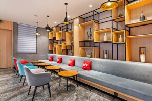 A modern lounge area with a grey sofa, colorful chairs, wooden tables, and shelves with decorative items. - Ibis Hotel Foshan Shunde Jing Long Subway Station (Foshan)