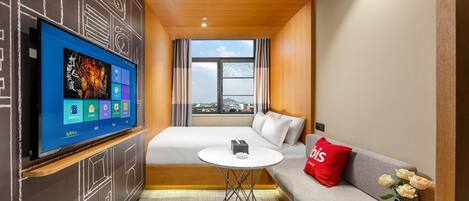 Una habitación de hotel con cama, sofá, televisor montado en la pared, una mesita y ventana con vista a la ciudad.