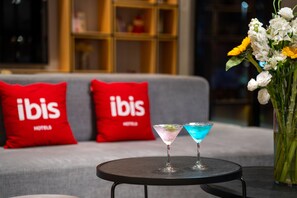 A room with a grey sofa, two red pillows with 'ibis' branding, a small round table with two martini glasses, and a vase with flowers. - Ibis Hotel Foshan Shunde Jing Long Subway Station (Foshan)