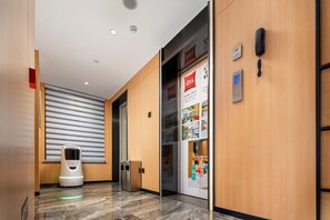 A hotel corridor with a self-service kiosk, a glass door with a poster, and a phone on the wall. - Ibis Hotel Foshan Shunde Jing Long Subway Station (Foshan)