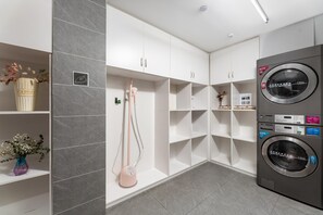 Un cuarto de lavado con lavadora de carga frontal, muebles blancos y un jarrón con flores sobre una repisa.