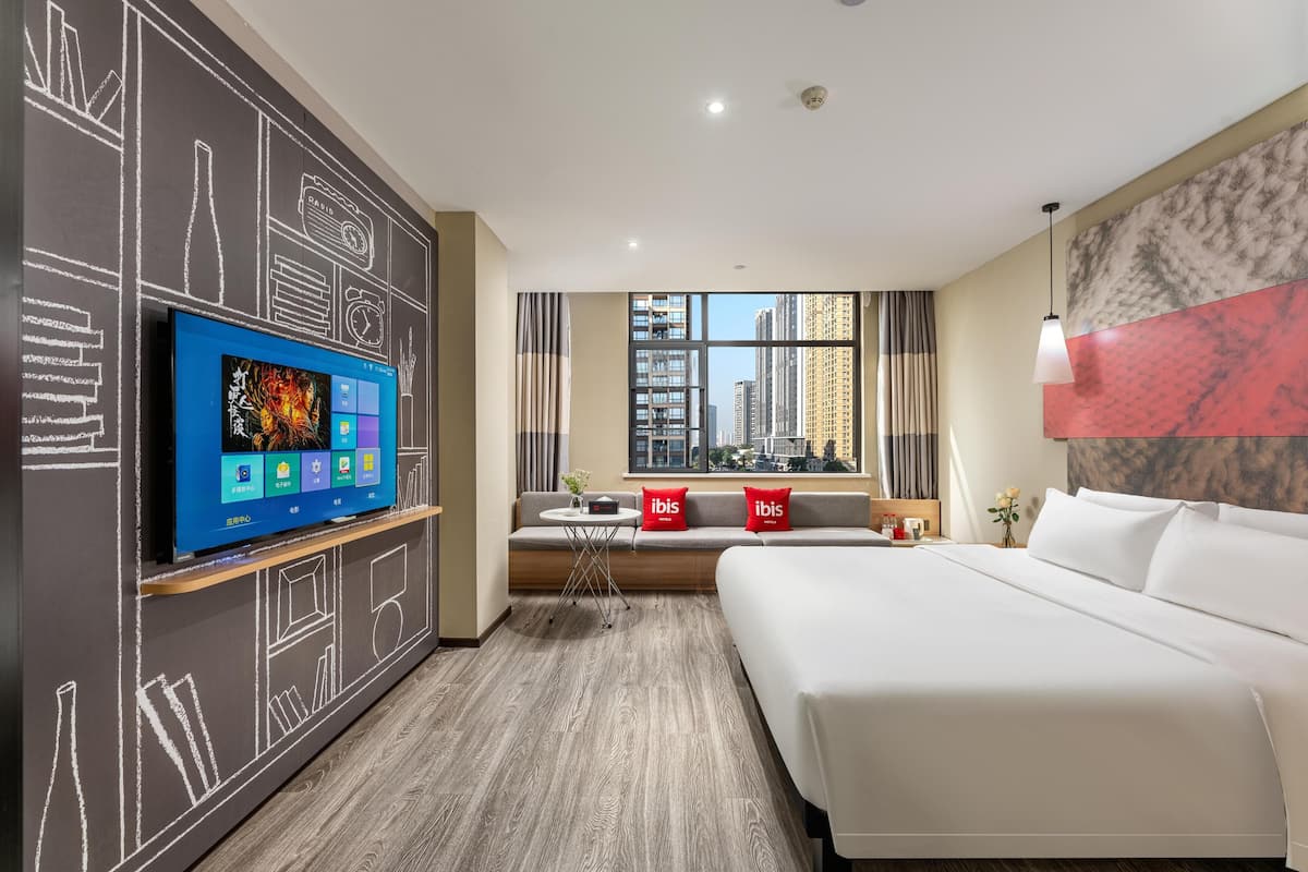 Habitación de hotel con una cama grande, un televisor sobre un mueble, una ventana con vista a la ciudad y una pared con diseño de pizarra.