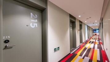 Corredor de hotel com carpete estampado, uma porta com a inscrição '215' e um sinal de saída de emergência.