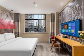 Habitación de hotel con cama, escritorio, televisión, ventana y vista a la ciudad.