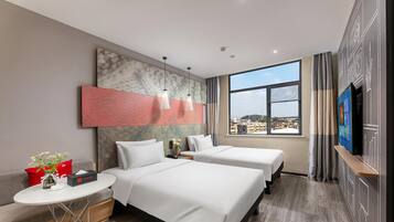 Hotelkamer met twee bedden, een tafeltje met een vaas, een televisie en een groot raam met uitzicht op de stad.