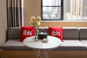 Habitación de hotel con sofá, una mesa redonda, un florero con flores y una caja de pañuelos.