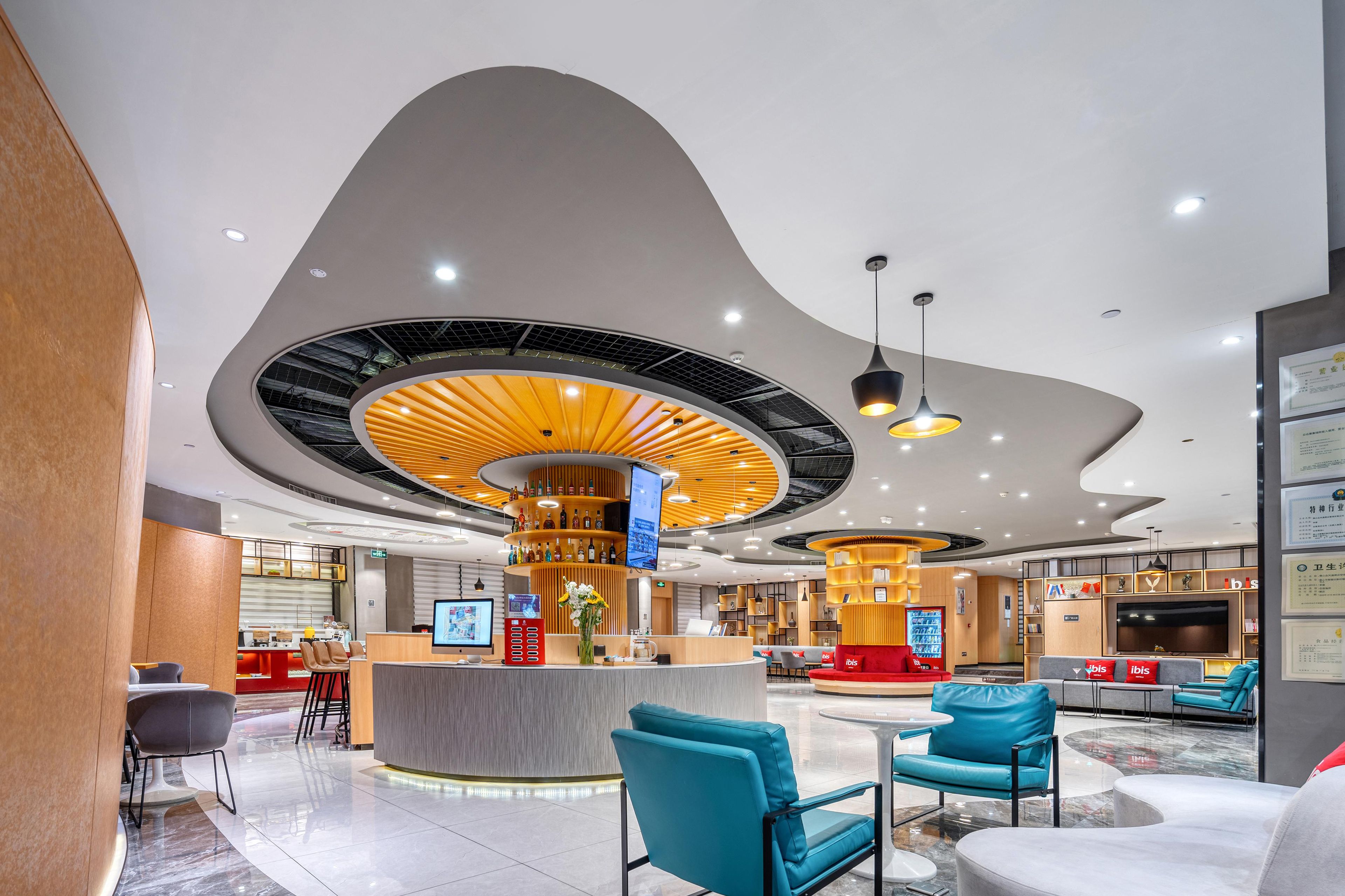 Un hall d’hôtel moderne doté d’un plafond incurvé, d’un bar central, de différents espaces aménagés avec des sièges et d’un comptoir de réception.