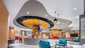 Een moderne hotel lobby met een gebogen plafond, een centrale bar, zitgedeeltes en een receptiebalie.