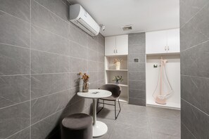 A modern bathroom with grey tiles, a white air conditioning unit, a small round table with a vase, a chair, and a shower area. - Ibis Hotel Foshan Shunde Jing Long Subway Station (Foshan)