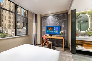 A hotel room with a large window, a desk with a computer, a chair, a bed, and a bathroom with a mirror and sink. - Ibis Hotel Foshan Shunde Jing Long Subway Station (Foshan)