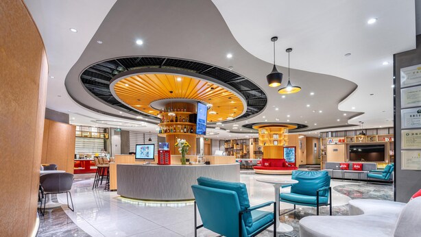 Eine moderne Hotelhalle mit gewölbter Decke, einer zentralen Bar, Sitzgelegenheiten und einer Rezeption.