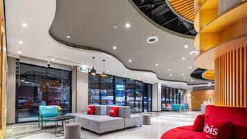 Een moderne hotellobby met zithoeken, een receptiebalie en grote ramen met uitzicht op de omgeving.