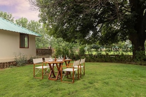 A patio with a table and chairs, a stone wall, and a building with a green roof. - Zana Forest Resort Ranthambore (Sawai Madhopur)