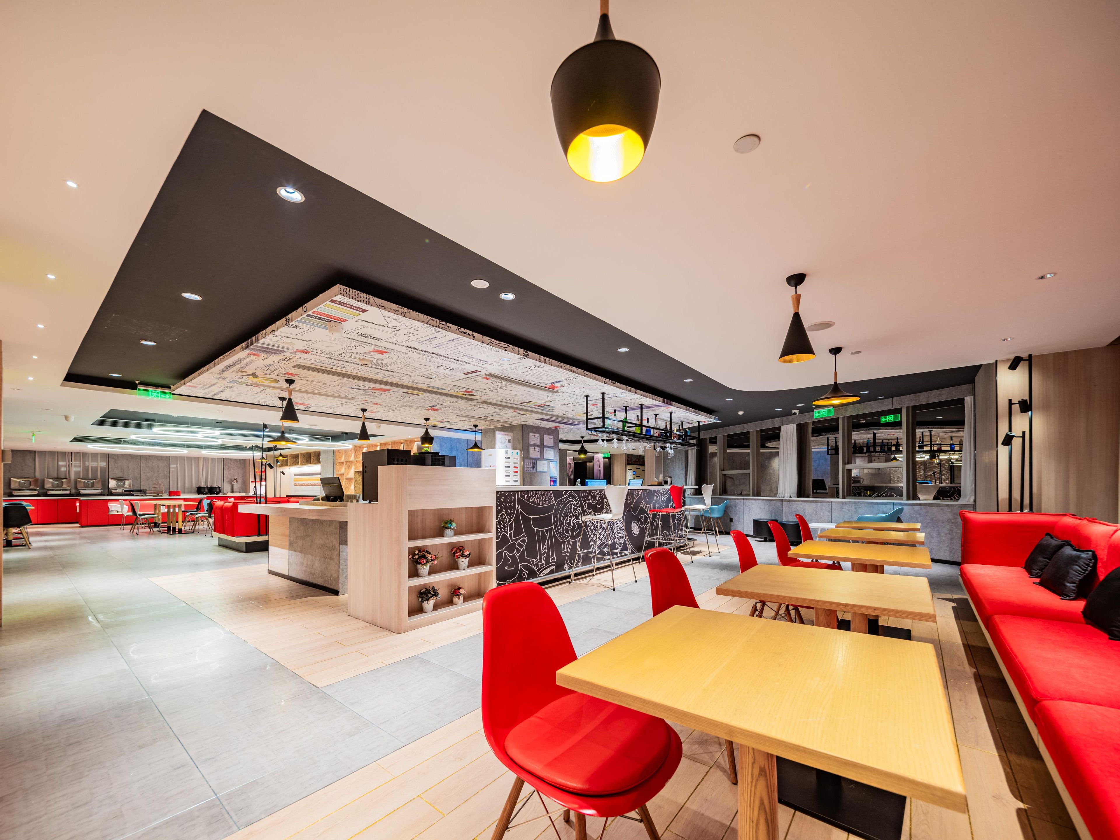 Un restaurant moderne avec des sièges rouges, des tables en bois et un plafond haut laissant apparaître les conduits.