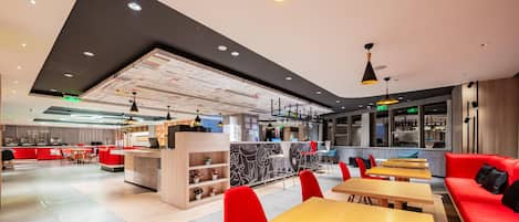 Un restaurant moderne avec des sièges rouges, des tables en bois et un plafond haut laissant apparaître les conduits.