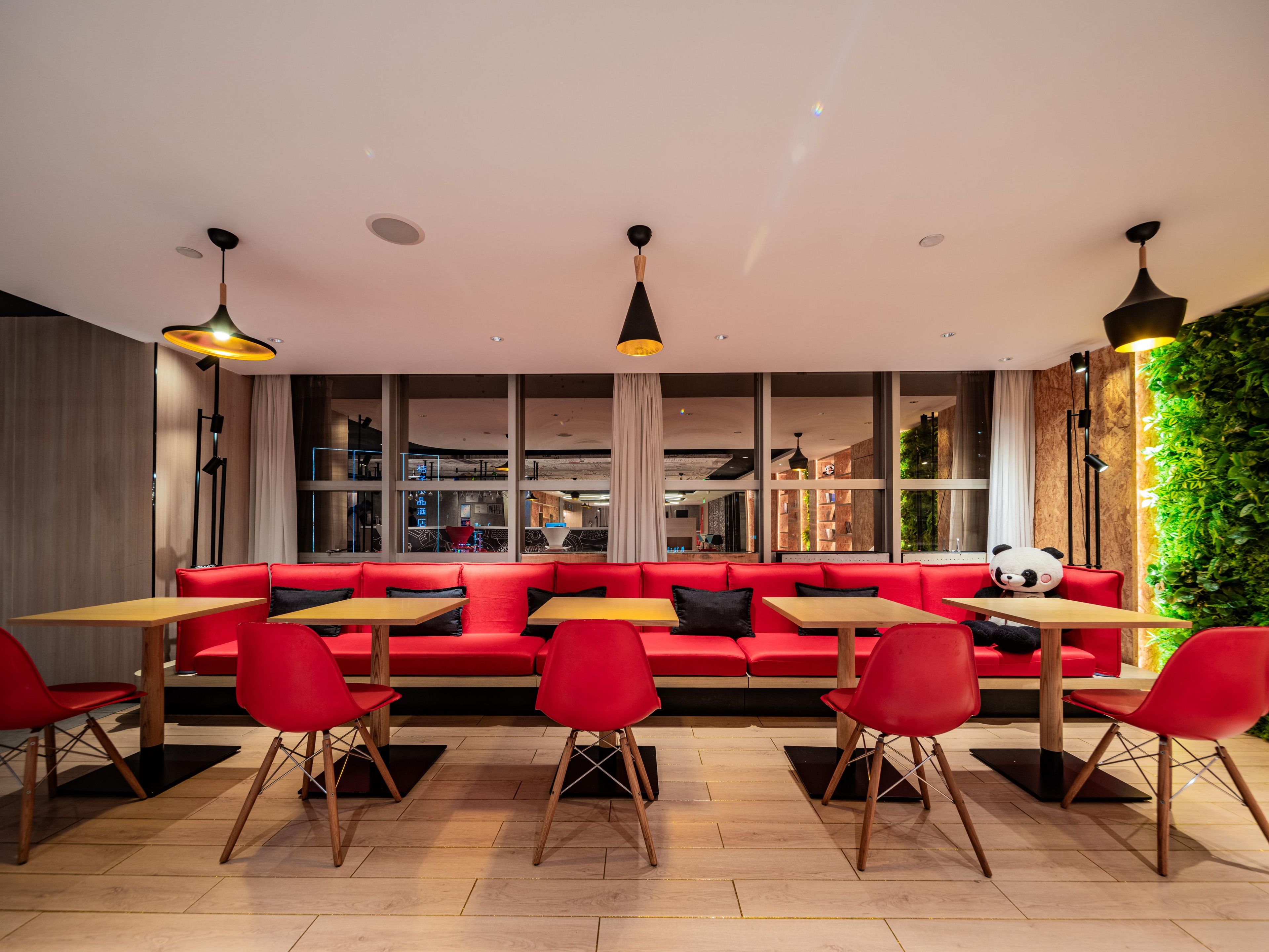 A modern restaurant with red seating, wooden tables, and pendant lighting.