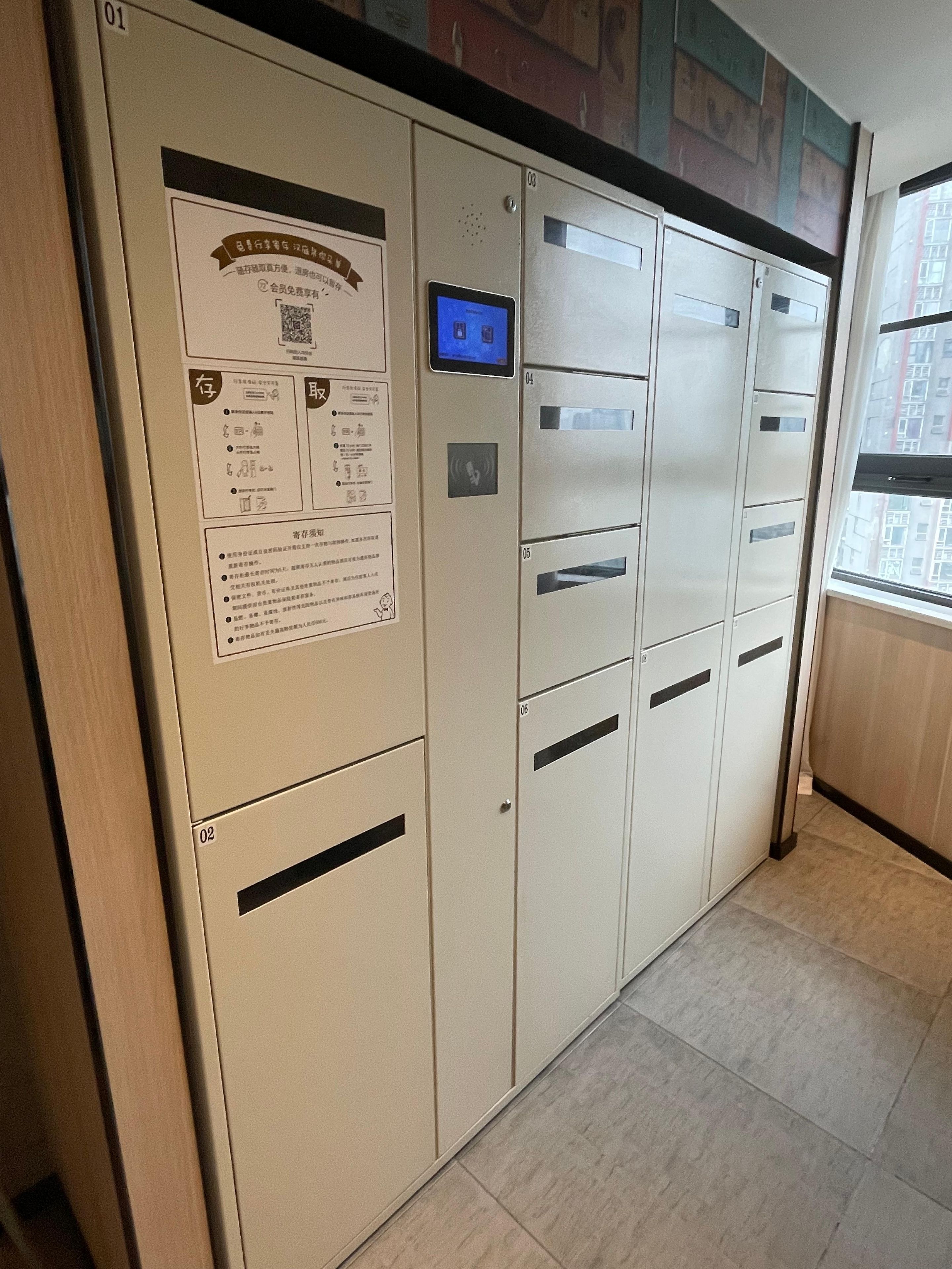 A row of beige lockers with numbered compartments, a digital display, and informational posters.