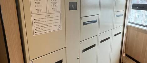 A row of beige lockers with numbered compartments, a digital display, and informational posters.