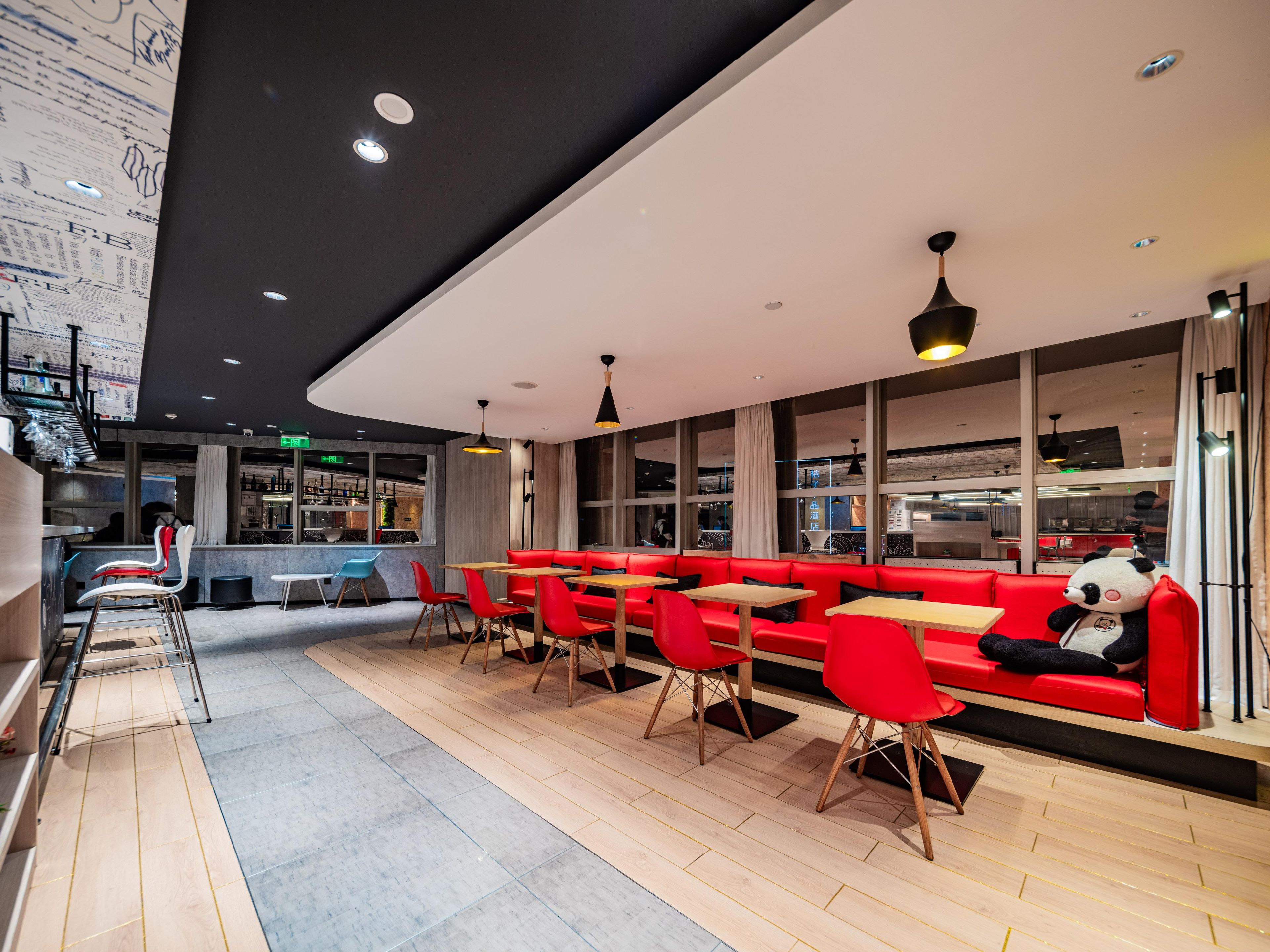 A modern restaurant with red seating, wooden tables, and a bar area.