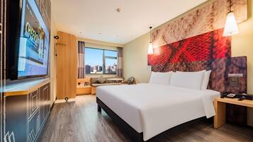 Habitación de hotel con una cama grande, televisor en la pared, vista a la ciudad y cabecera moderna.