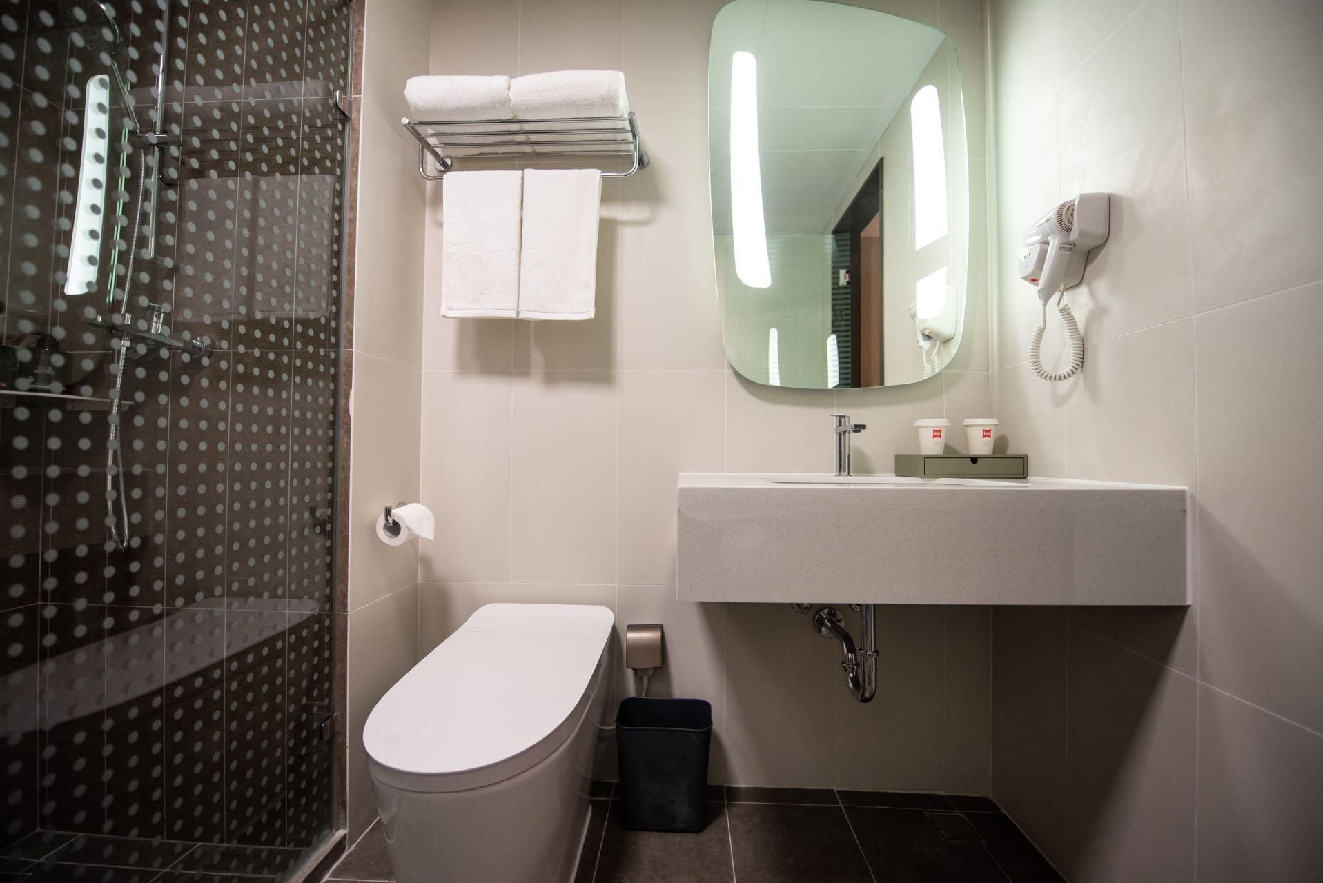 A bathroom with a toilet, a sink, a mirror, a towel rack, and a shower area.
