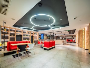 Un interior modern amb una zona d'estar vermella, un taulell i un panell de menús digital.