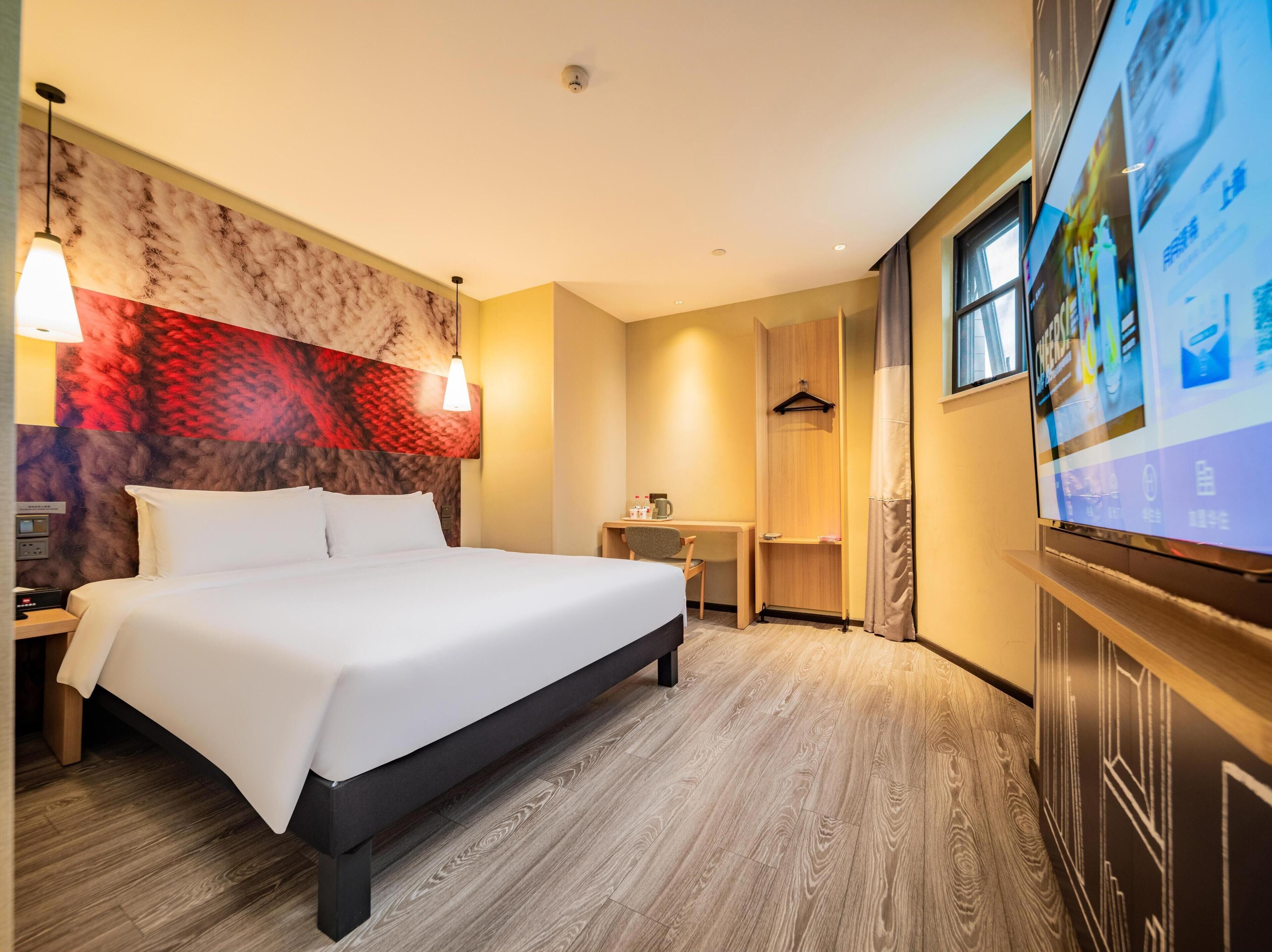 Hotelkamer met een bed, nachtkastje, lamp, televisie en een muur met een rood-beige patroon.