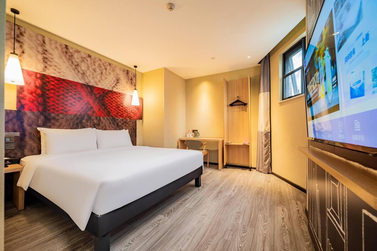 Una habitación de hotel con cama, mesita de noche, lámpara, televisor y una pared con diseño rojo y beige.