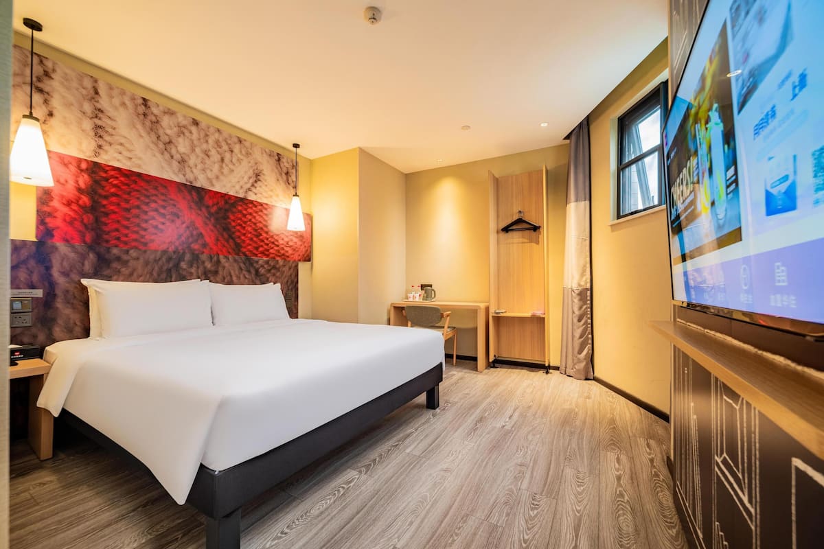 Hotelkamer met een bed, nachtkastje, lamp, televisie en een muur met een rood-beige patroon.