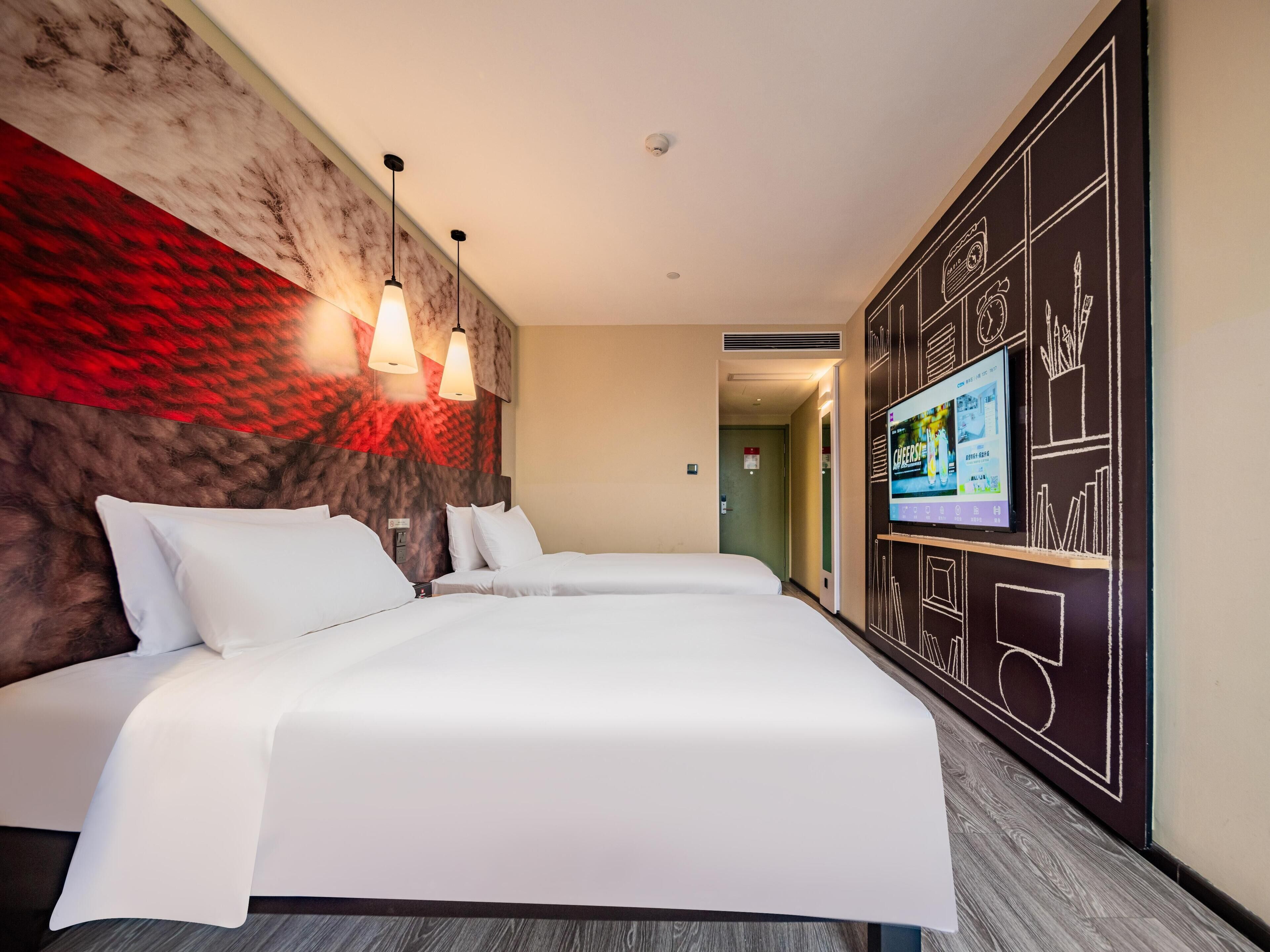 Een hotelkamer met een groot bed, twee bedlampen, een televisie aan de muur en een wand met een roodbruine textuur.