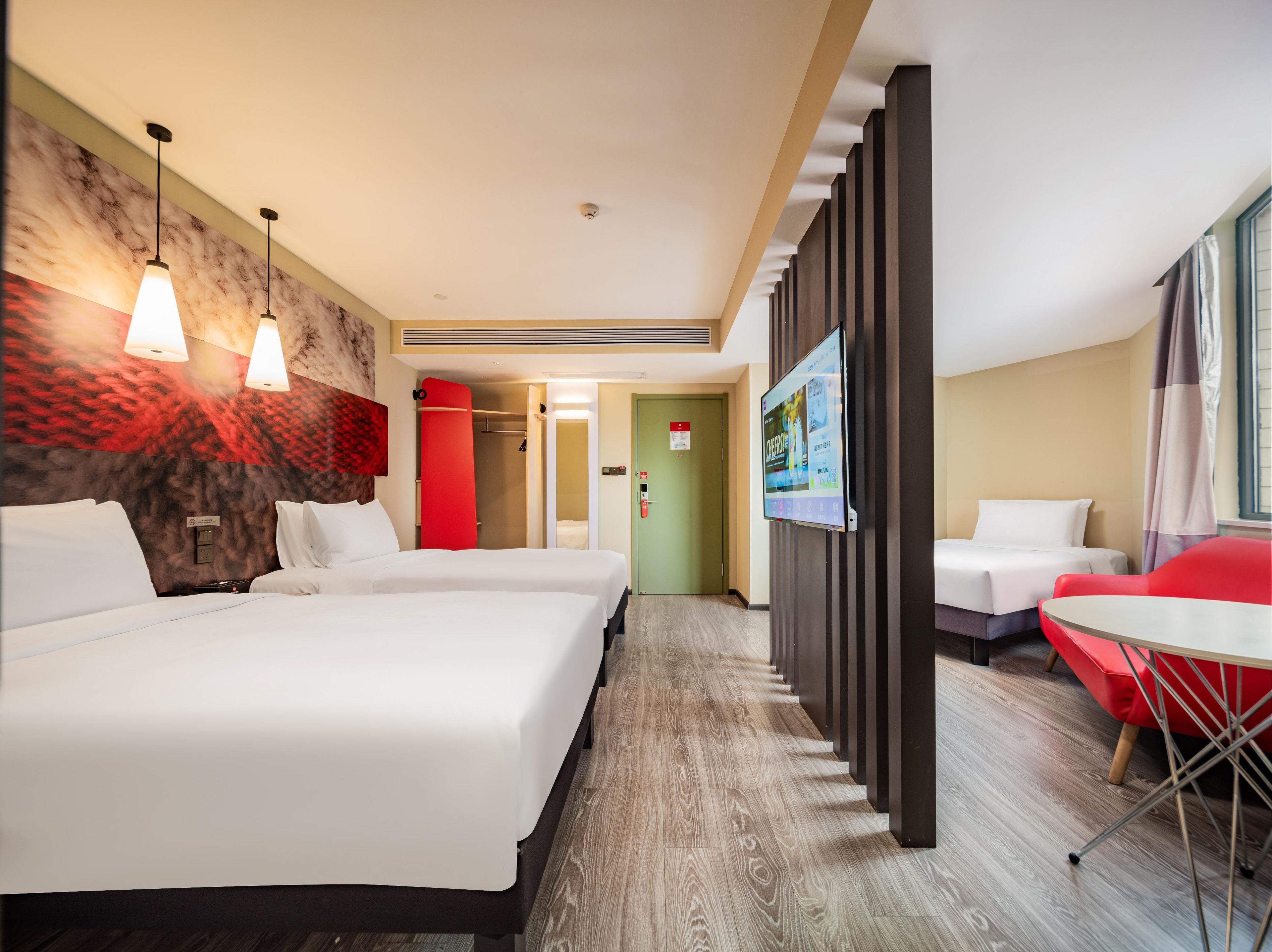 A hotel room with two beds, a TV, a red chair, and a small table.