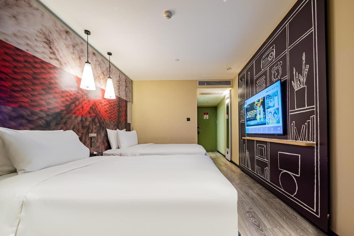 Una habitación de hotel con dos camas, un televisor en la pared y un mural.