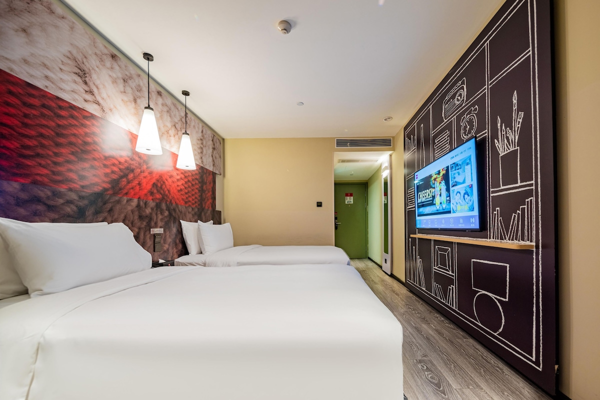 A hotel room with two beds, a TV on the wall, and a mural.