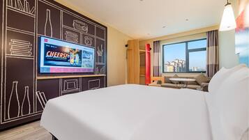 Habitación de hotel con una cama grande, un televisor mostrando un anuncio, vista a la ciudad a través de la ventana y un diseño moderno con paredes de pizarra.