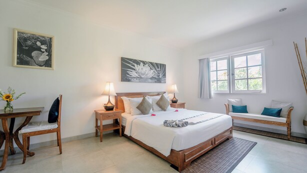 A bedroom with a bed, bedside tables, a desk, a chair, a bench, and artwork on the walls. - Umalas Suites Bali (Kerobokan)