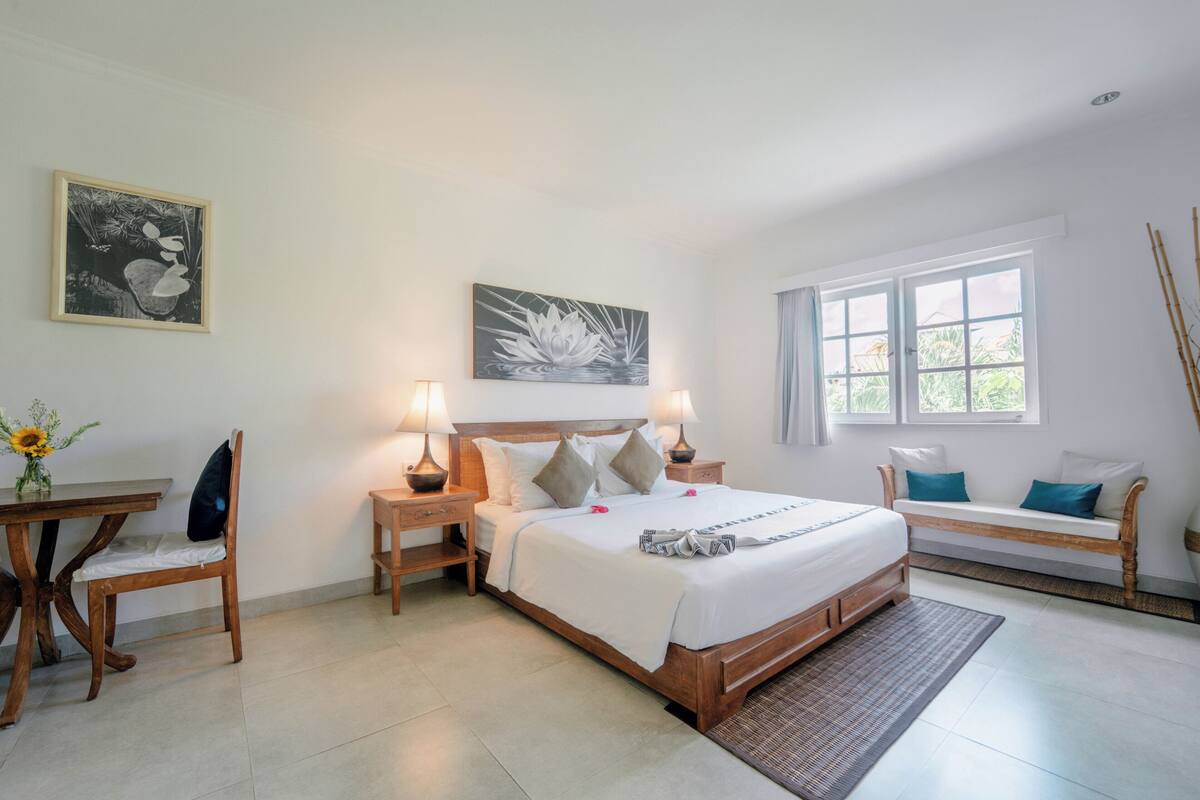 A bedroom with a bed, bedside tables, a desk, a chair, a bench, and artwork on the walls.