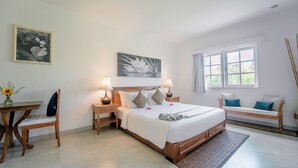 A bedroom with a bed, bedside tables, a desk, a chair, a bench, and artwork on the walls. - Umalas Suites Bali (Kerobokan)