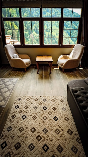 Una habitación con dos sillones, una pequeña mesa de madera y vistas a un bosque a través de amplios ventanales.