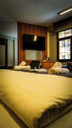 Un cuarto de hotel con una cama, un televisor de pantalla plana montado en la pared, una ventana con vista y un cabecero de madera.