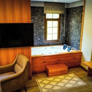 Un baño con una bañera de madera, una silla de madera, un televisor montado en la pared y una ventana con vistas al exterior.