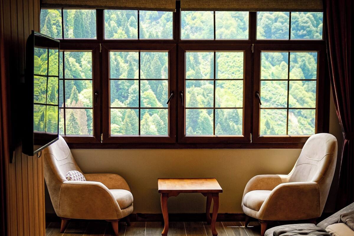 Ein Zimmer mit großem Fenster, zwei Sesseln, einem kleinen Tisch und einer Couch.